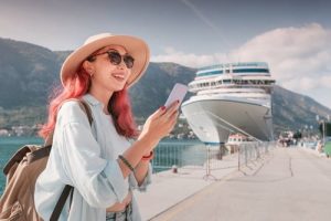 young woman using smartphone on cruise ship dock wearing hat and backpack
